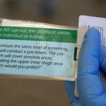A TSA agent displays a laminated card printed with the text of what agents are required to say to any passengers who "opt out" of full-body scan security procedures.